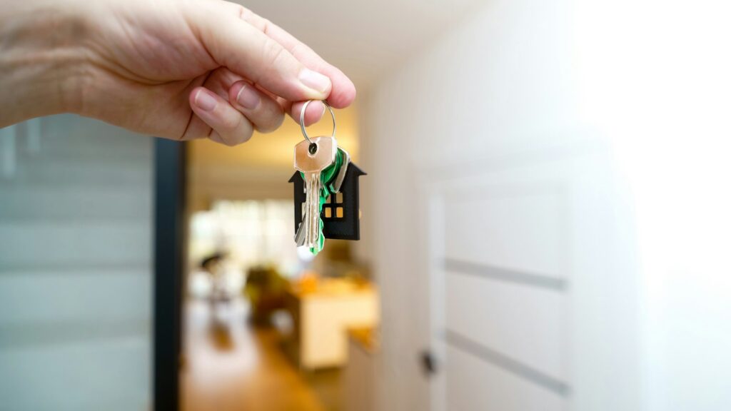 Consegna delle chiavi di casa con portachiavi a forma di casetta, cambio gestore affitti brevi